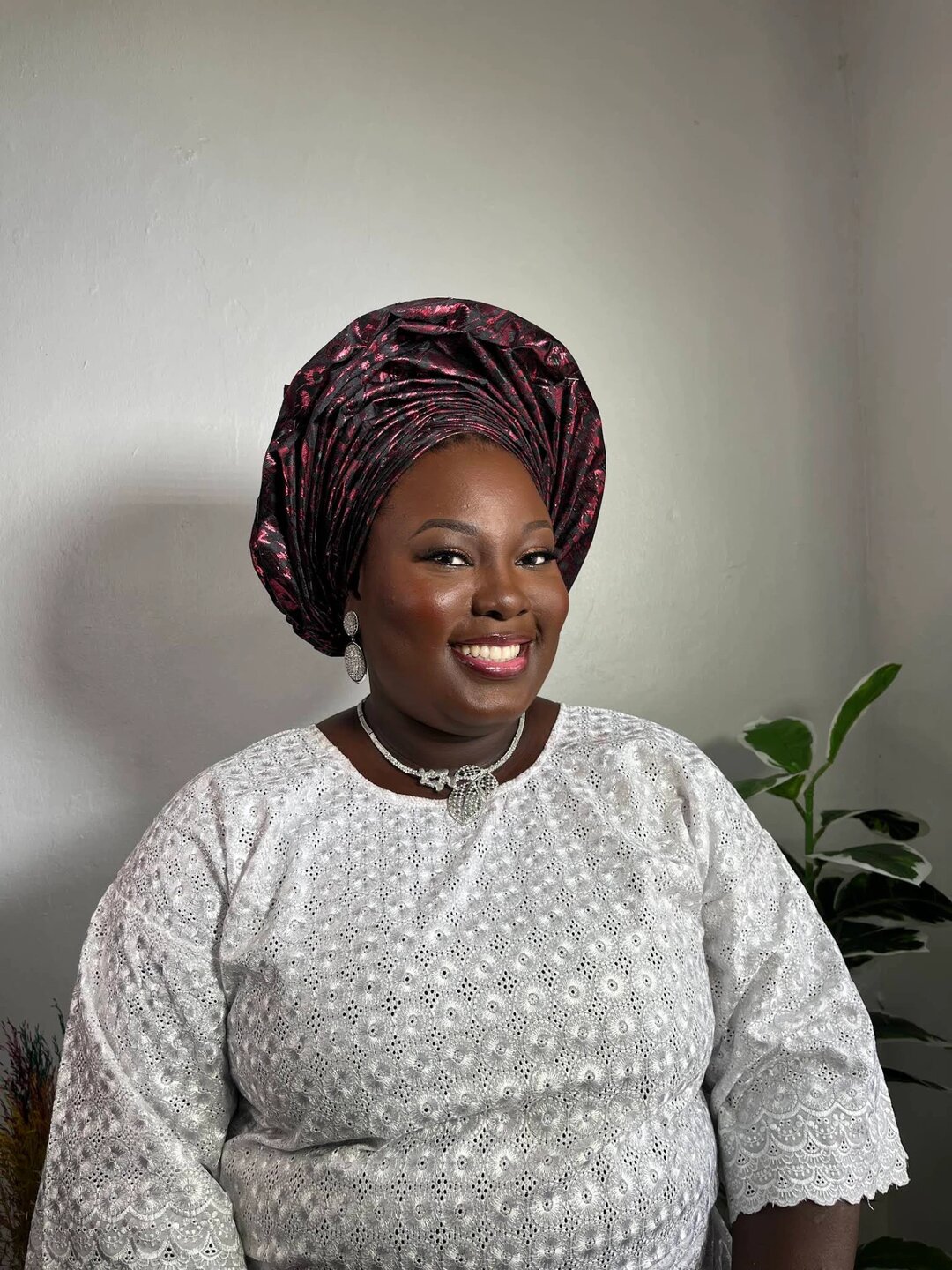Client in a silver lace outfit and burgundy gele with occasion makeup